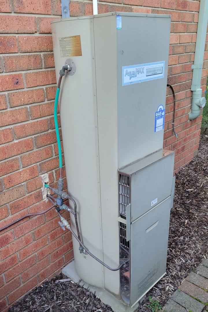 Old gas storage hot water system on a brick wall before replacement